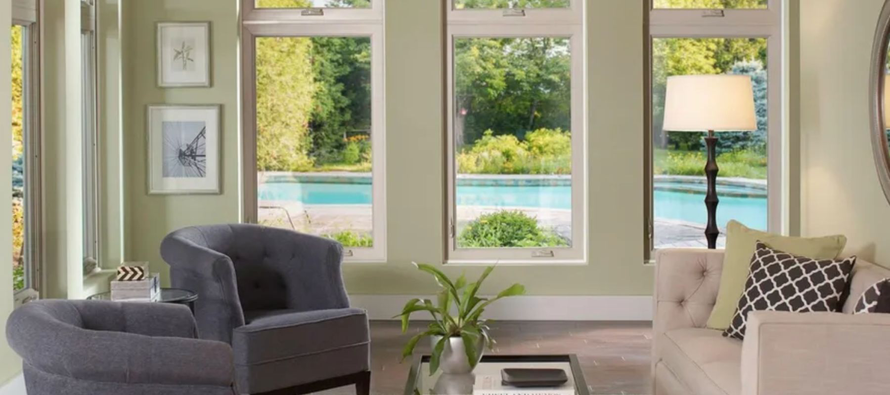 Bright living room with multiple vertical windows overlooking a pool and lush greenery
